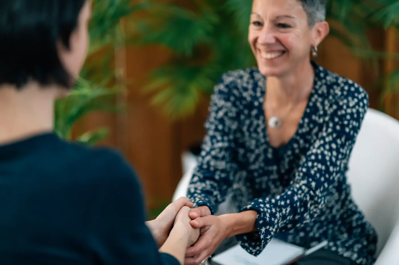 Female counsellor smiles and holds hands of woman