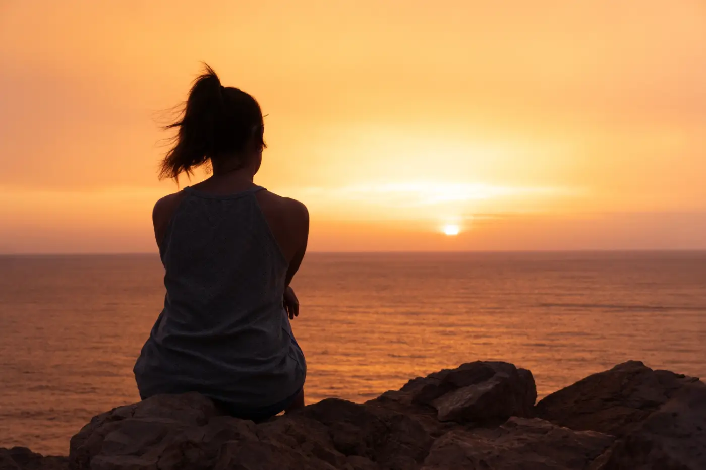 Woman sitting on beach wall gazing at sunset